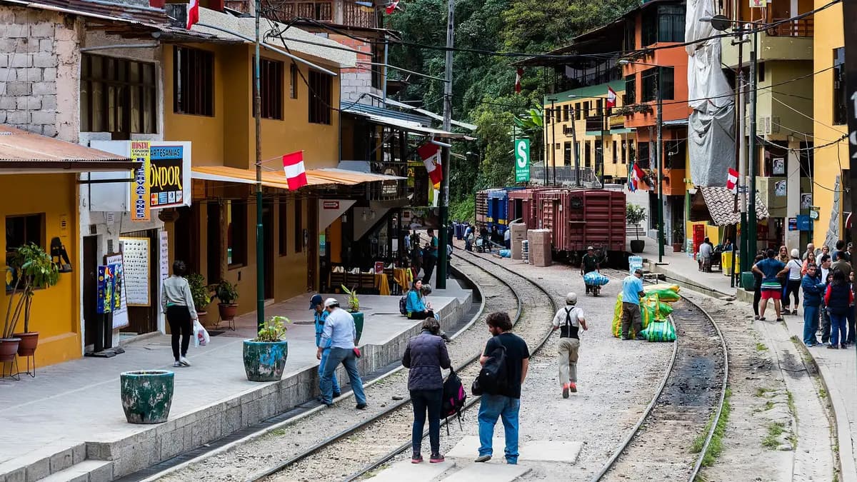 Calle de Aguas Calientes con la línea del tren al centro y turistas caminando entre hoteles