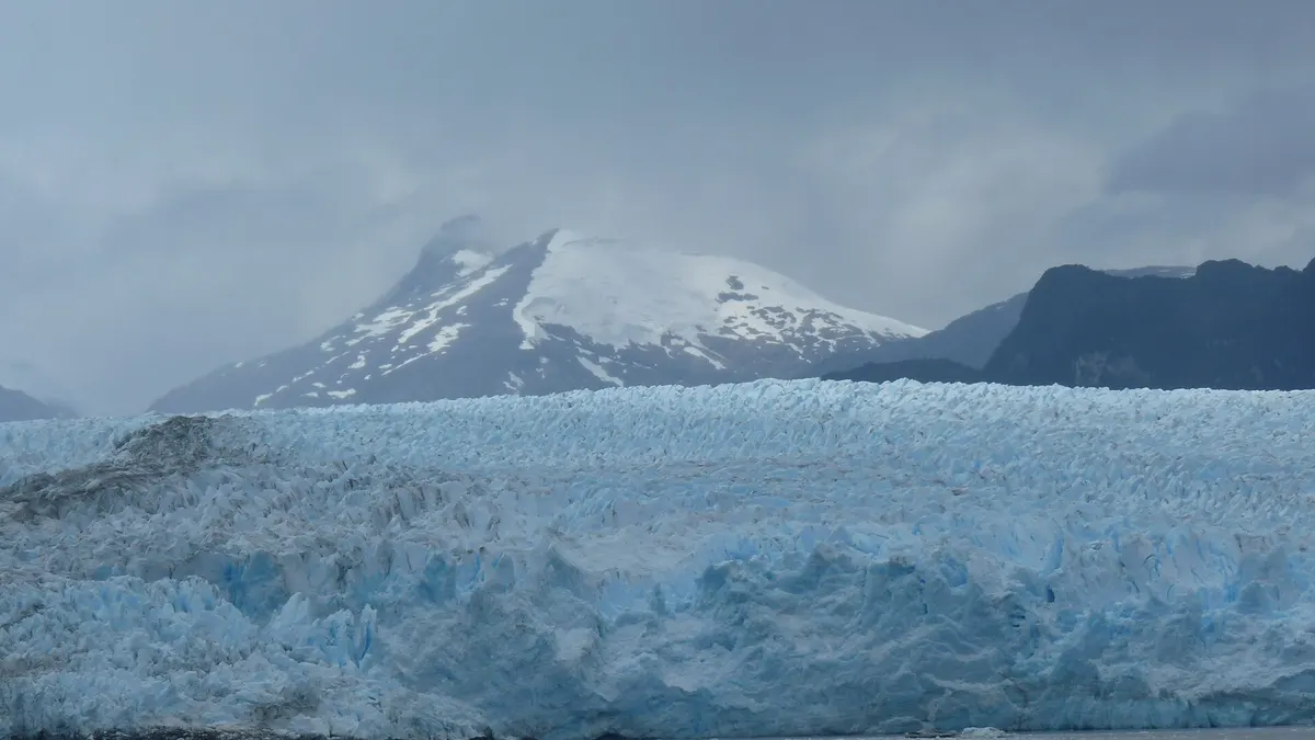 Pared de hielo azulado del glaciar Pío XI con una cumbre nevada al fondo