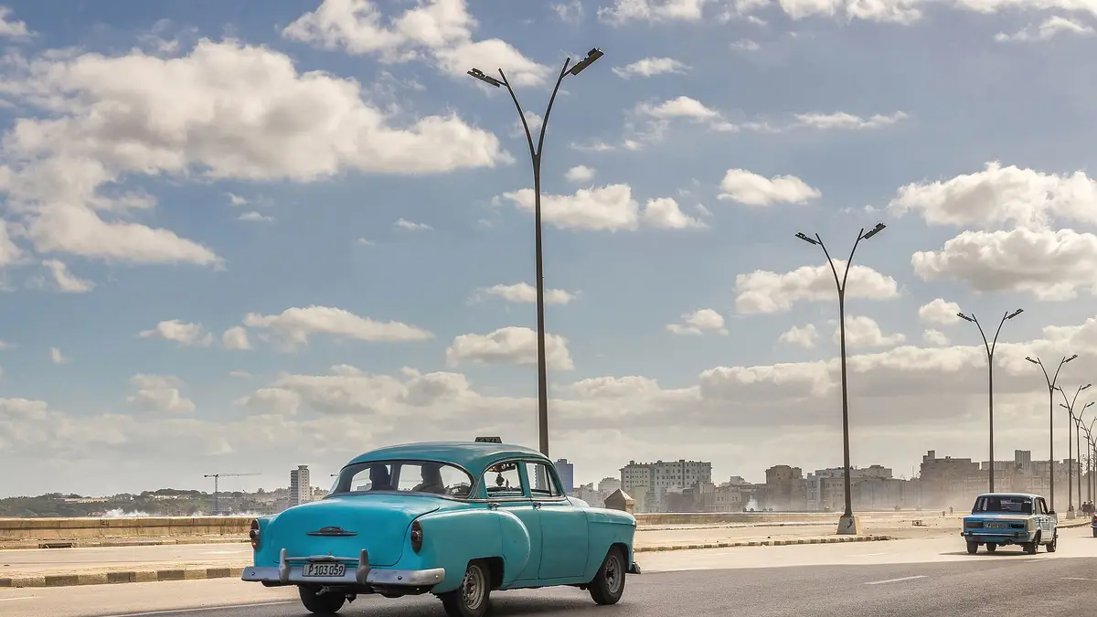 Auto clásico de color celeste circulando por el Malecón de La Habana con el mar a la derecha