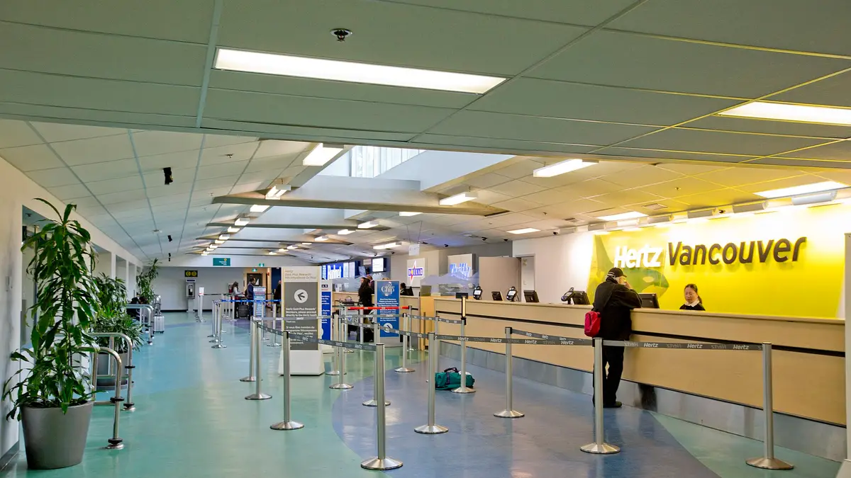 Mesón de arriendo de autos en el hall de un aeropuerto con letreros amarillos y filas ordenadas
