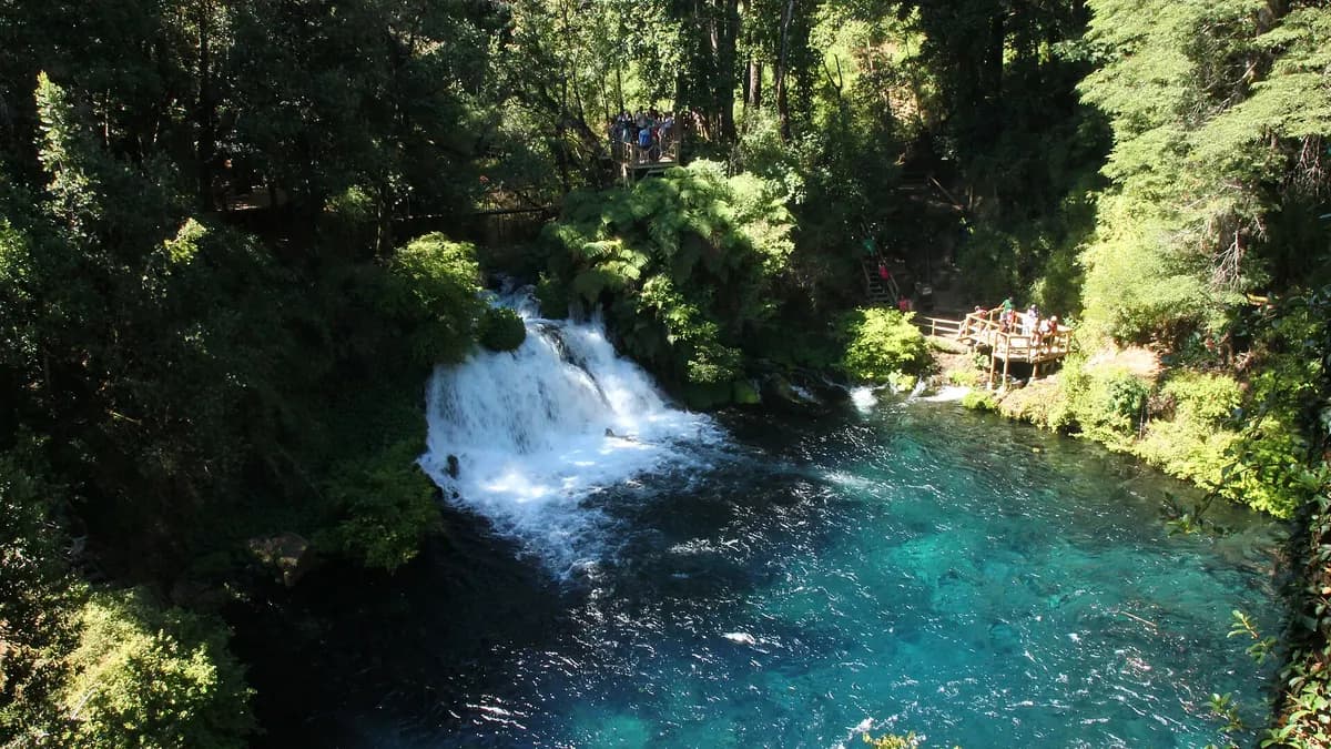 Salto de agua cayendo a una poza turquesa rodeada de vegetación en Caburgua