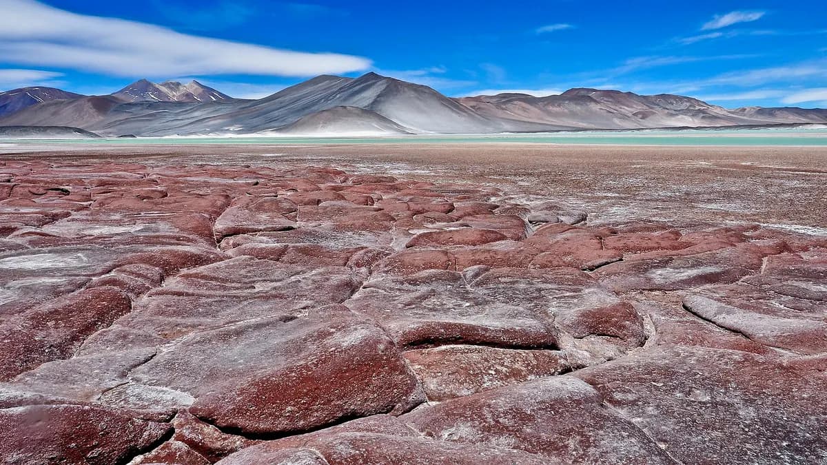 Bloques de roca color óxido en la orilla del salar con agua y sal detrás