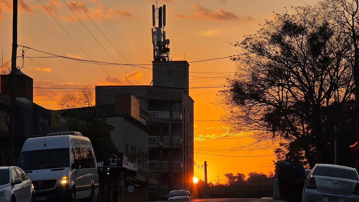 Amanecer naranjo sobre una avenida de Puerto Iguazú con autos estacionados