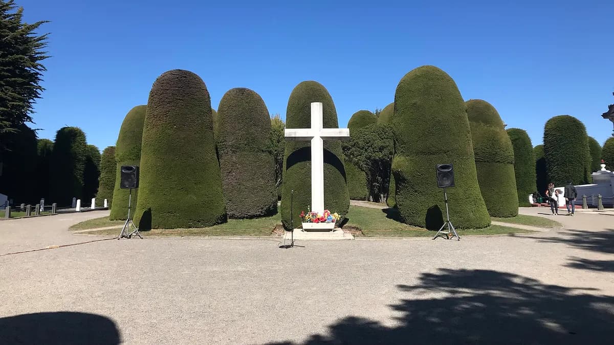 Hileras de cipreses podados y una cruz blanca en el acceso al cementerio de Punta Arenas