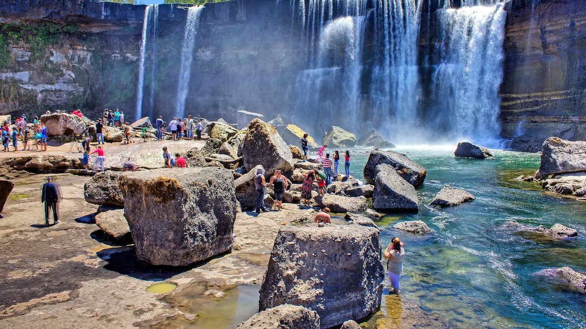 Turistas parados en las rocas frente a la caída de agua del río Laja