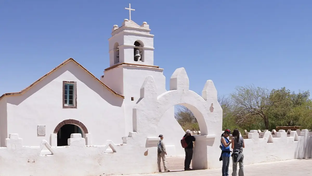 Iglesia blanca de adobe de San Pedro de Atacama con su campanario y turistas en la entrada