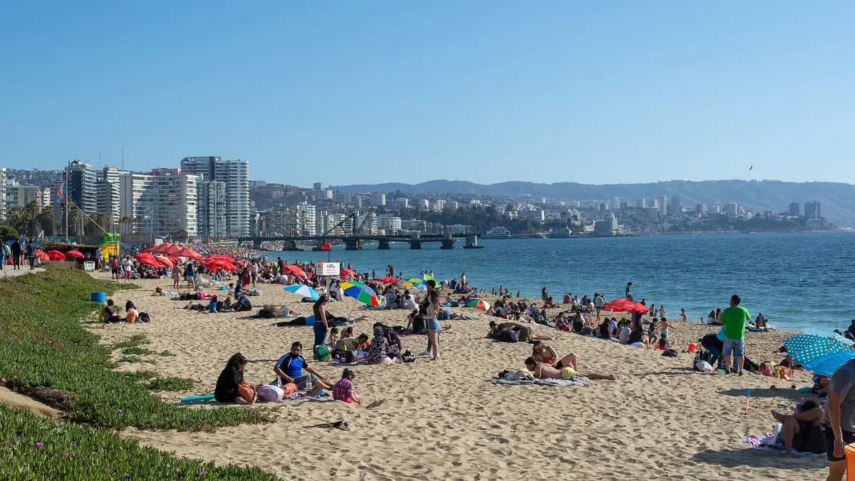 Gente tomando sol en la arena con edificios frente a la costa de Viña del Mar
