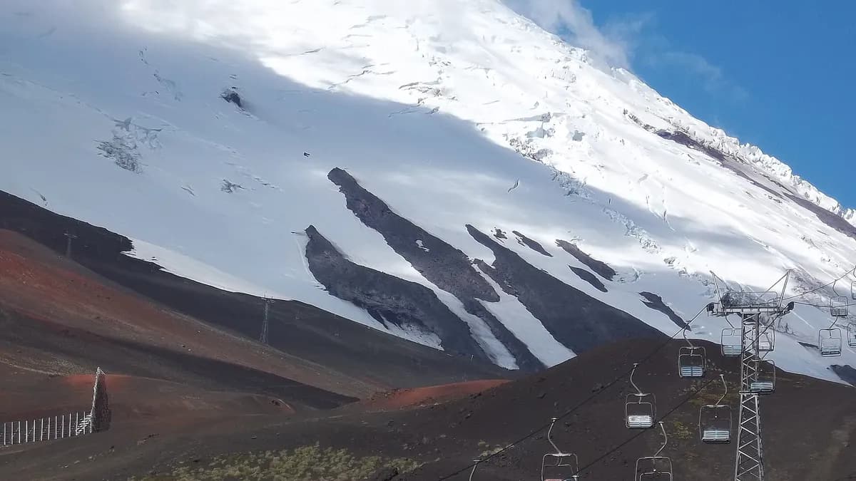 Línea de aerosillas subiendo por una ladera de nieve y roca rojiza del Osorno